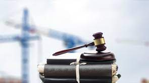 Gavel on legal books, construction cranes behind.